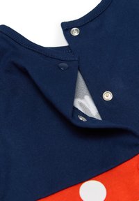 Chemise à manches courtes bleu marine avec un bas rouge à pois blancs. Fermetures à pression et à bouton au niveau du cou. Texture de tissu douce.