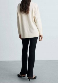 Tricot crème avec un ourlet côtelé, associé à un pantalon évasé noir à côtes et des sandales à talons présentant un design de bride.
