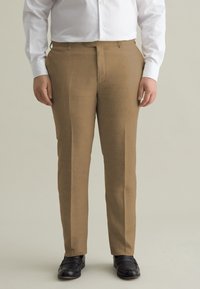 Pantalons en lin marron avec un devant plat, des jambes droites et des passants de ceinture, associés à des chaussures noires et une chemise blanche à boutons.