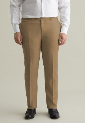 Pantaloni in lino marrone con frontale piatto, gambe dritte e passanti per cintura, abbinati a scarpe nere e a una camicia bianca con bottoni.