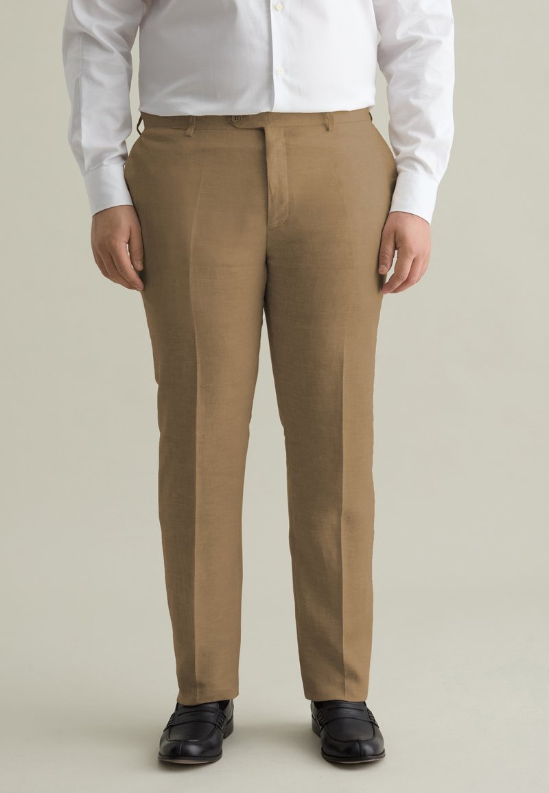 Pantalons en lin marron avec un devant plat, des jambes droites et des passants de ceinture, associés à des chaussures noires et une chemise blanche à boutons.