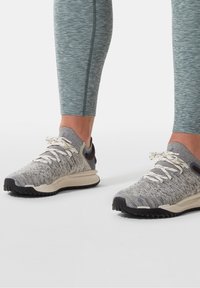 Šedé sportovní boty s texturovaným pleteným svrškem, bílými tkaničkami, kontrastní černou podrážkou a tmavými akcenty na patě.