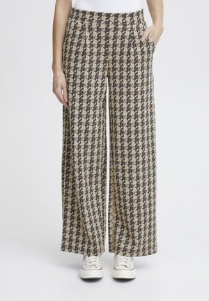 Brede broek in een houndstooth-patroon, met zwart en beige kleuren, een gestructureerde stof en zijzakken. Gecombineerd met witte sneakers.