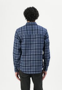 Camisa de cuadros azul marino de algodón con cuello abotonado, mangas largas y dobladillo recto, que presenta acentos en azul claro en el patrón.