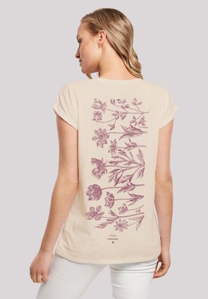 Beige T-Shirt mit einem floralen Design in Mauve auf dem Rücken, mit kurzen, aufgerollten Ärmeln und einem lockeren Schnitt. Geschmeidige Baumwolltextur.