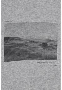 Camiseta gris con un gráfico texturizado negro de líneas onduladas y el texto "Perspectiva", con una cita debajo, todo impreso en suave material de algodón.