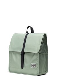 Groene nylon rugzak met een klepafsluiting, zwarte band en witte logopatch. Beschikt over een vierkante vorm en een gladde textuur.