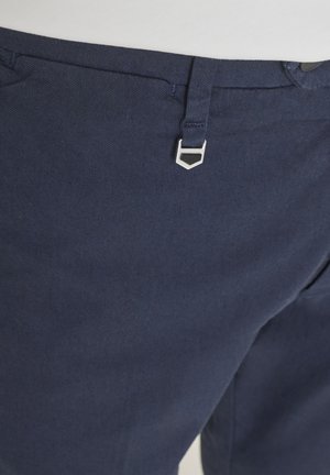 Primo piano di pantaloni blu navy con passante per cintura che presenta un piccolo dettaglio decorativo in metallo argento e nero.