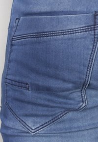 Jeans in denim di blu medio, caratterizzati da una tasca a patch curvata con dettagli a doppia cucitura e una texture liscia.
