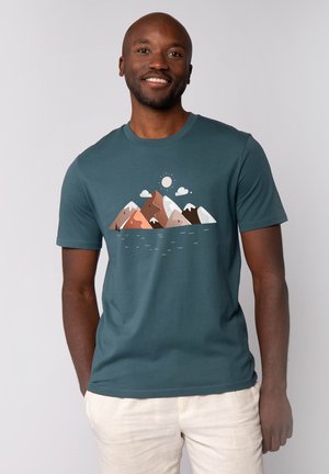 Teal katoenen t-shirt met een bergafbeelding in verschillende aardetinten, met een zon en wolken erboven, zachte textuur en een ronde hals.