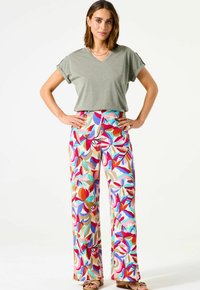 Camiseta gris de cuello en V combinada con pantalones de pierna ancha multicolores que presentan un patrón floral en rojo, rosa, azul y beige. Sandalias planas.