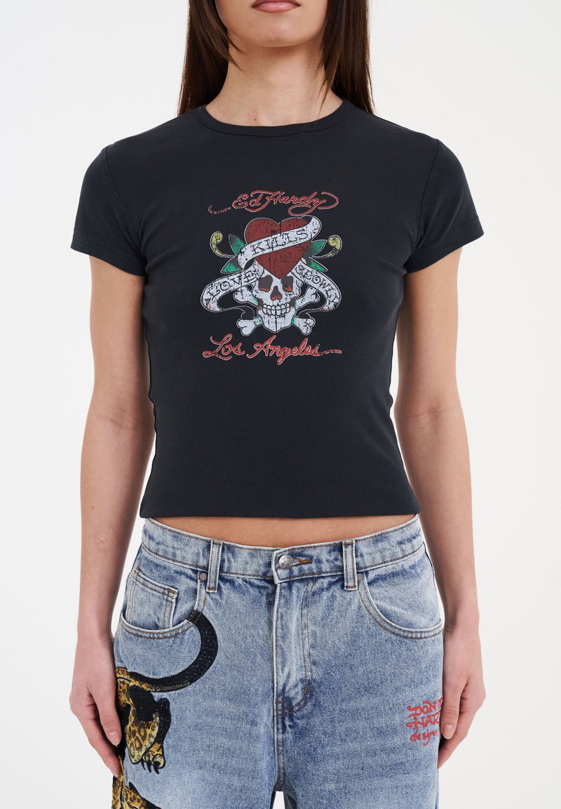 Black cotton t-shirt with short sleeves, featuring a colorful skull graphic and text design. Paired with light blue denim jeans with animal accents.