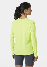 Langsleeve sportshirt in fel neon geel, met raglanmouwen en een textuurstof. Gekleed met donkergrijze shorts.