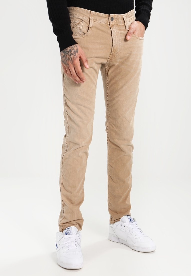 Beige corduroy pants with a slim fit, featuring pockets, subtle texture, and a classic 5-pocket design, paired with white sneakers.