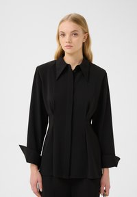 Blusa nera a maniche lunghe con colletto strutturato, design frontale plissettato e polsini leggermente svasati, realizzata in tessuto morbido.