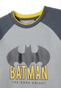Camisa gris y gris oscuro con cuello amarillo, que presenta un gran logo negro de Batman y el texto amarillo "BATMAN" con "THE DARK KNIGHT" abajo.