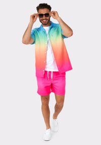 Button-up shirt with a blue to pink gradient, paired with bright pink shorts. Model wears white sneakers and sunglasses.