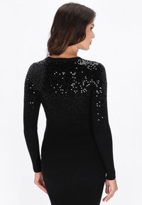 Schwarzes, geripptes Kleid mit langen Ärmeln, das an den Schultern einen Farbverlauf aus Pailletten aufweist und einen strukturierten, funkelnden Effekt erzeugt.