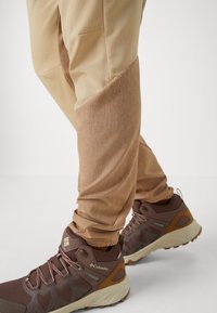 Beige vandringsbyxor med en texturerad design och sidofickor, kombinerat med bruna vandringsskor som har mesh- och gummidetaljer.