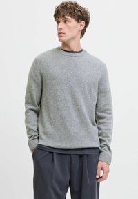 Pull gris à col rond en tricot fin, avec des poignets et un ourlet côtelés, associé à un pantalon sombre. Design simple avec une coupe décontractée.