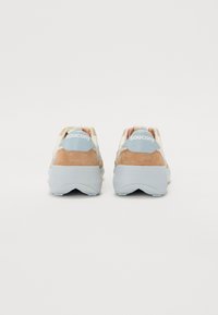 Saucony-sneakers med en beige semsket overdel, lyseblå aksenter og hvite såler. Har en hæltab og logo bak.