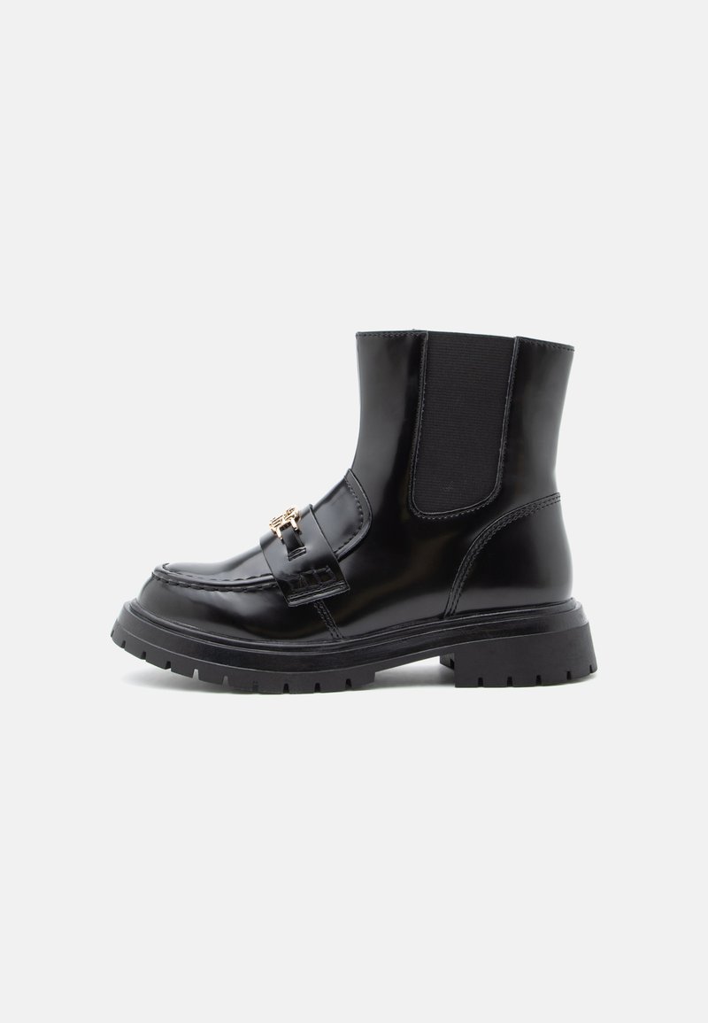 Bottine en cuir noir avec semelle épaisse, panneaux latéraux élastiques, couture moc-toe et boucle dorée décorative sur fond blanc.