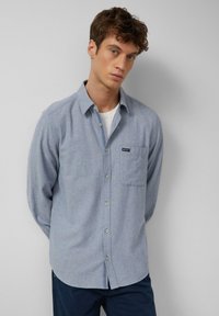 Camicia button-up azzurra con una texture sottile, maniche lunghe e una tasca sul petto con un piccolo logo del brand.