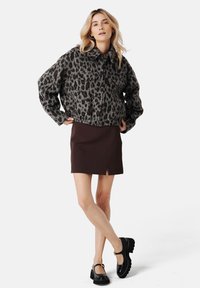 Kurtka w panterkę, oversize, szara, z zamkiem z przodu i spiczastym kołnierzem; zestawiona z brązową mini spódnicą i czarnymi butami na platformie.