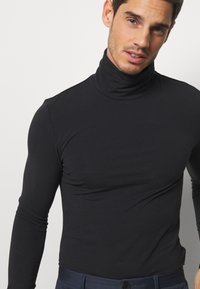 Camiseta negra de manga larga tipo cuello alto, hecha de un tejido elástico, con un diseño ajustado y una textura suave.