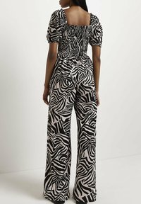 Czarny i biały kombinezon w zebrę z bufkowymi rękawami i marszczonym tyłem. Szerokie nogawki zwiększają komfort i swobodę ruchów.