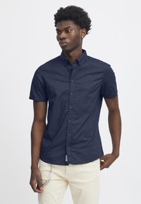 Srajca na kratke rokave, z gumbi, v mornarsko modrem blagu. Ima klasičen ovratnik, slim fit in subtilno teksturo s temnimi gumbi.