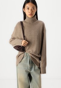 Pruun suuruse turtleneck-sviiter pehmes kootud materjalis, millel on soonikkoes käised ja ääred. Kanda kergelt siniste kõrge vöökohaga teksade ja väikese pruuni kottiga.