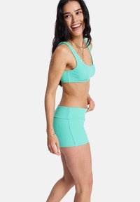Un ensemble de sport deux pièces en bleu sarcelle texturé, composé d'un crop top à encolure dégagée et d'une jupe courte assortie avec une taille cintrée et un design sans coutures.