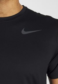 Camiseta atlética negra hecha de una tela suave y ligera. Presenta un escote redondo y un sutil logo de Nike en gris en el hombro izquierdo.