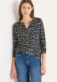 Marineblå bluse med lange ærmer og beige abstrakt mønster, v-udskæring og blødt stof, kombineret med lyseblå jeans. Glat tekstur, afslappet pasform.