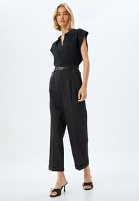 Maglietta nera a maniche corte con colletto, abbinata a pantaloni neri a vita alta e a gamba larga. Accessoriata con una sottile cintura nera e scarpe con tacco aperte.