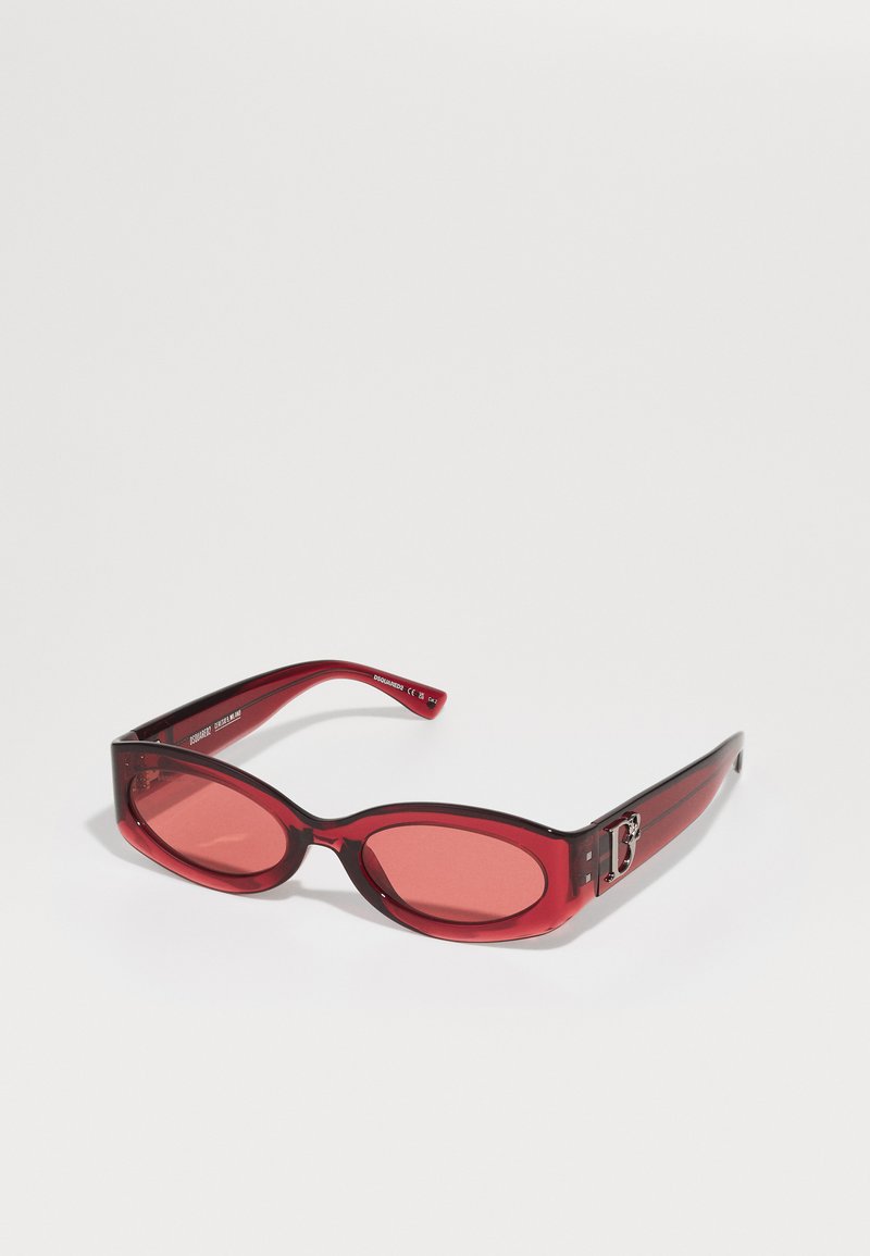 Red sunglasses with a glossy finish and oval-shaped lenses. Features a sleek black accent near the hinge and engraved branding on the arm.