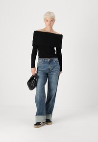 Črn top brez naramnic z rebrastim vzorcem, modri široki jeans z uničenimi robovi, črna torba in črno-bele superge. Minimalističen dizajn.