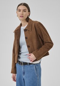 Brown suede cropped jacket with large collar, three buttons, and side pockets, paired with a light blue shirt and high-waisted jeans.