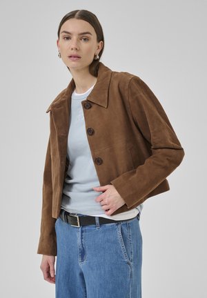 Brown suede cropped jacket with large collar, three buttons, and side pockets, paired with a light blue shirt and high-waisted jeans.
