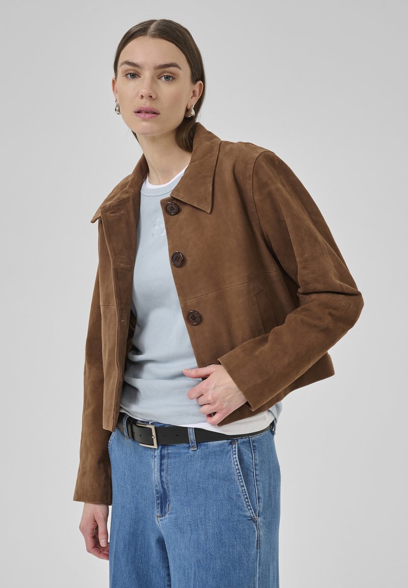 Brown suede cropped jacket with large collar, three buttons, and side pockets, paired with a light blue shirt and high-waisted jeans.