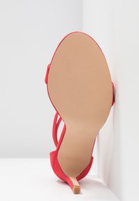 Escarpin rouge à talon haut avec un dessus en tissu doux, dos ouvert et un talon élancé. La semelle est lisse et légèrement texturée pour une meilleure adhérence.