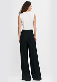 Czarne spodnie z szerokimi nogawkami i wysokim stanem o gładkiej fakturze, zestawione z białym topem bez rękawów. Stylizacja jest prosta i dopasowana.