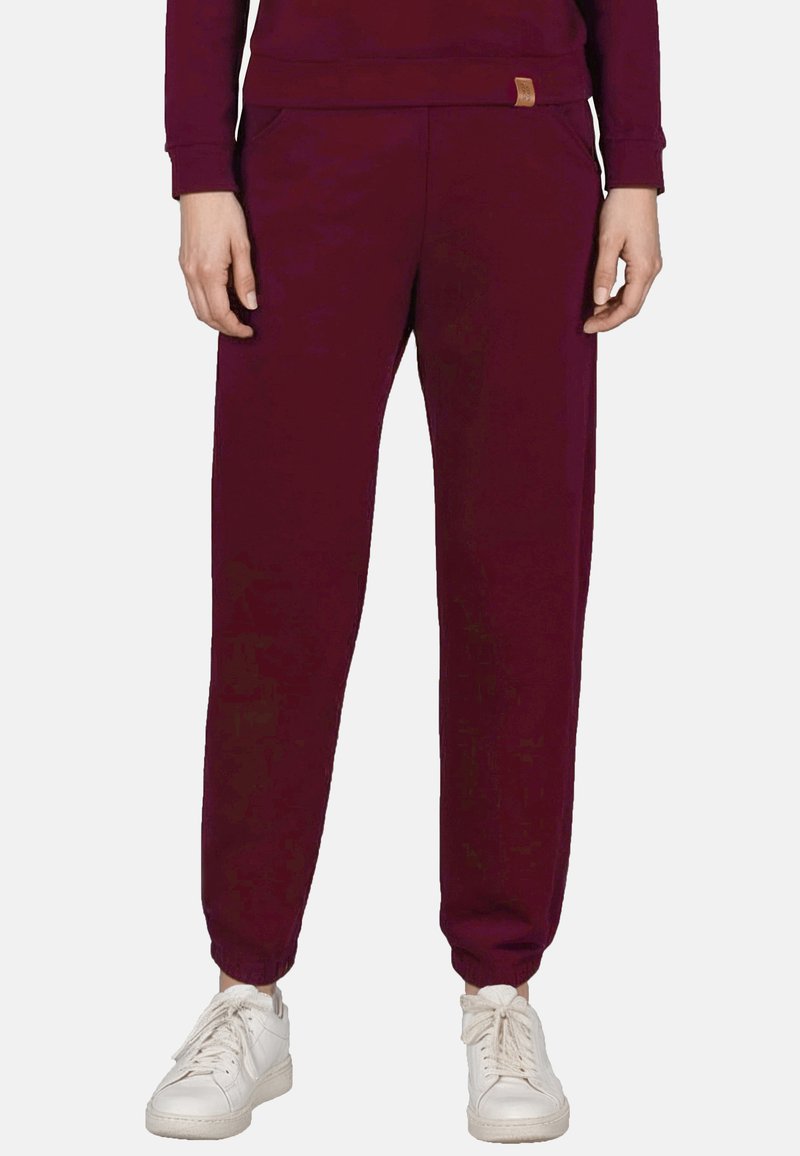 Bordeaux joggers gemaakt van zachte stof met een elastische tailleband, zijzakken en manchetten aan de enkels, gecombineerd met witte sneakers.