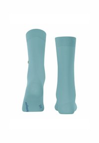 Chaussettes bleu clair présentées à la verticale, montrant les bords côtelés et le design sans coutures. Le logo de la marque est visible sur le côté.