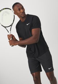 Camiseta y pantalones cortos deportivos Nike negros, con un diseño de cuello en V, textura suave, y con un logo swoosh blanco en el pecho y el lateral.