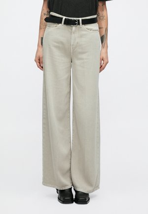 Ανοιχτό γκρι τζιν παντελόνι με φαρδιά μπατζάκια και ομαλή υφή, με μπροστινές τσέπες και μαύρη ζώνη. Φορεμένο με μαύρα μποτάκια αστραγάλου.