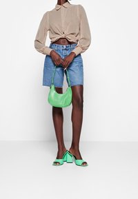 Blusa beige a pois, annodata in vita; shorts di denim; borsa a spalla in pelle verde; sandali verde con tacco quadrato e punte aperte.