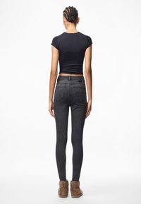 Černé přiléhavé tričko s krátkými rukávy spojené s tmavě opranými úzkými džíny a hnědými kotníkovými botami. Má zadní kapsy a jednoduchý design.