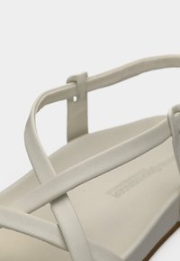 Άσπρο δερμάτινο σανδάλι με χιαστί λουριά, επίπεδη σόλα και μινιμαλιστικό σχέδιο. Διαθέτει απαλό υφή και καθαρές γραμμές.